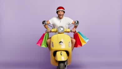 cheerful guy with helmet shopping bags driving yellow scooter